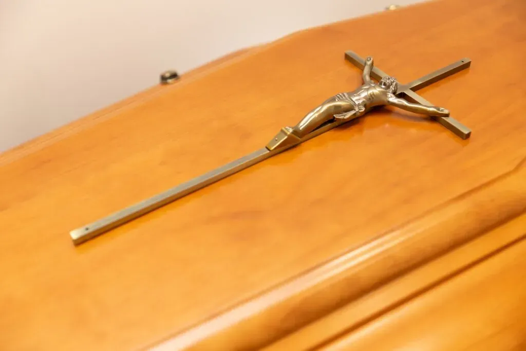 Cercueil en bois clair surmonté d'un crucifix en métal.
