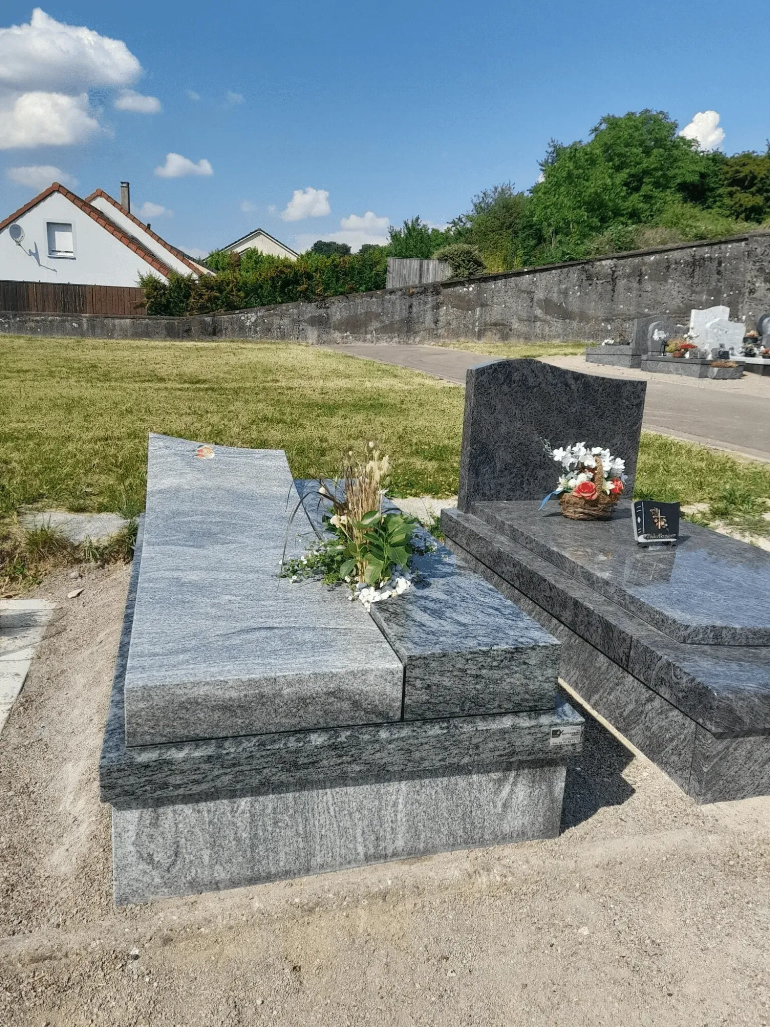 Monument funéraire double en granit gris clair avec composition florale.