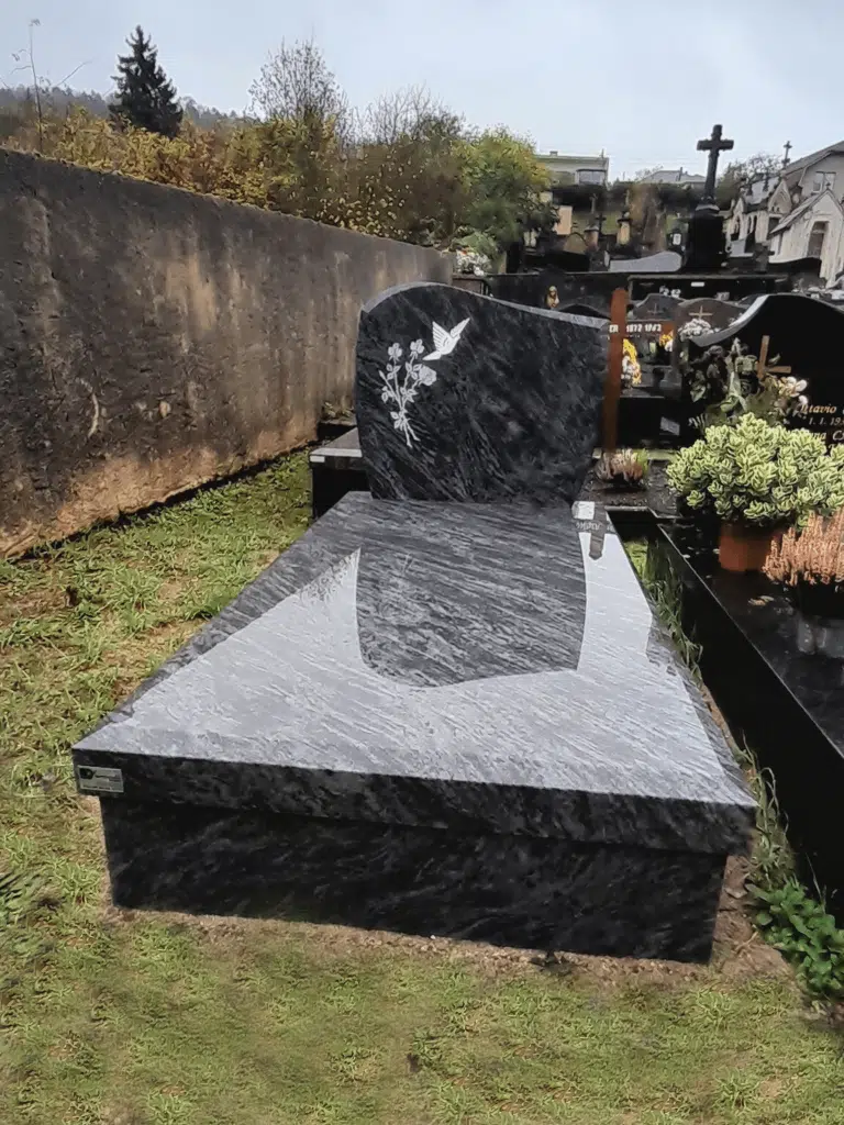 Monument funéraire en granit bleu nuit gravé d'une colombe blanche.