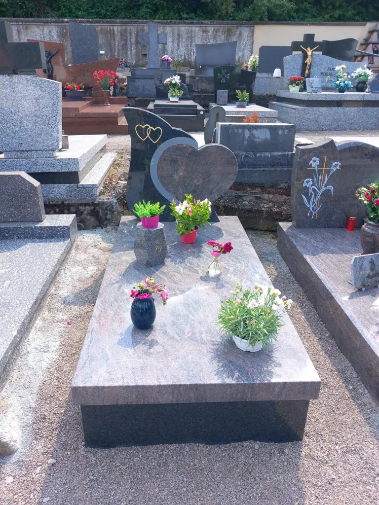 Tombe en granit gris garnie de fleurs fraîches avec stèle en forme de cœur.