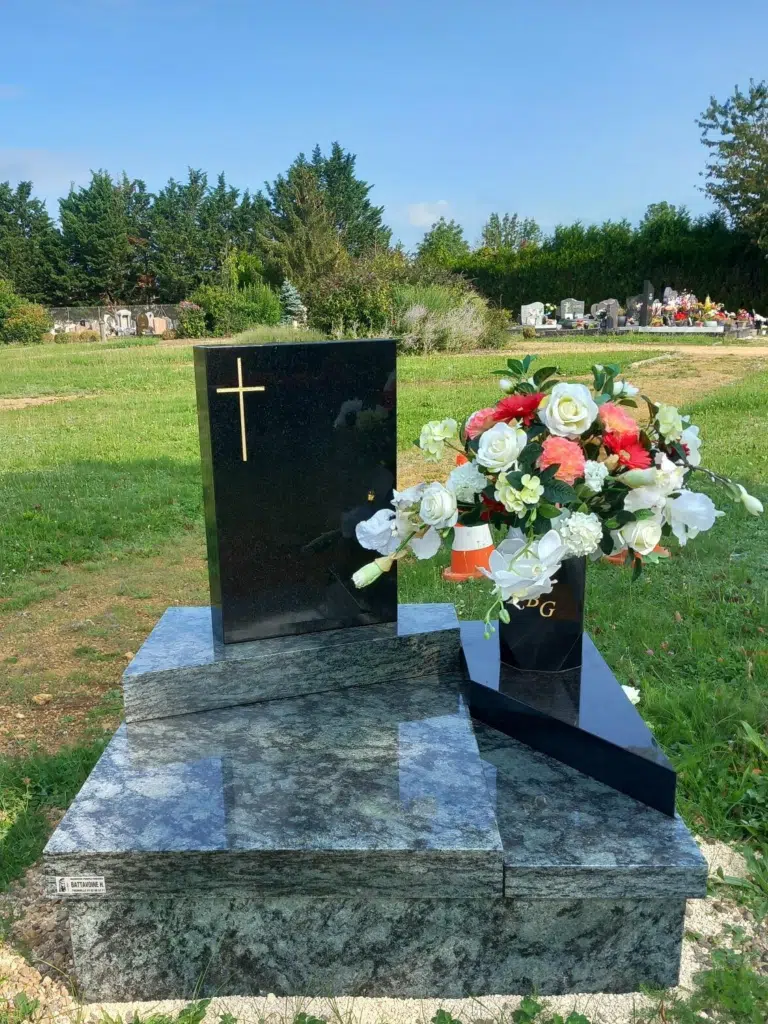 Monument cinéraire moderne en granit noir et gris orné d'un bouquet de fleurs.